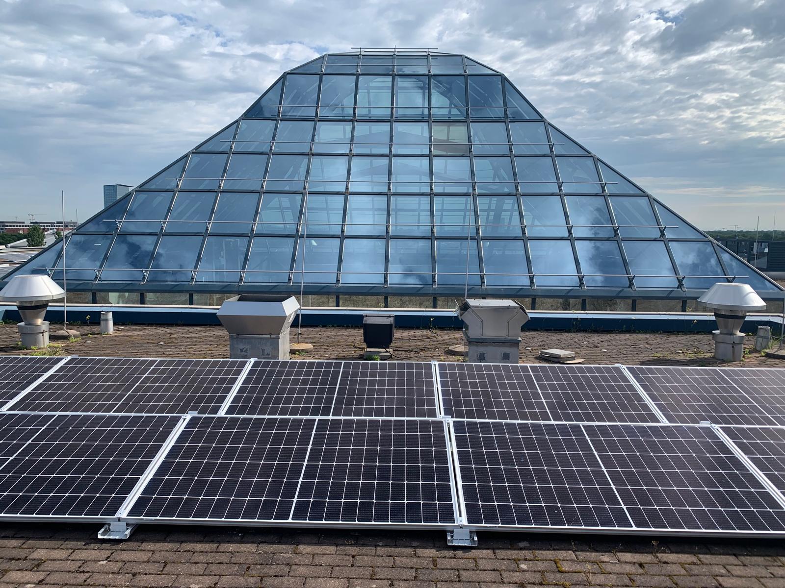 Photovoltaikanlage auf Flachdach vor moderner Glaspyramide